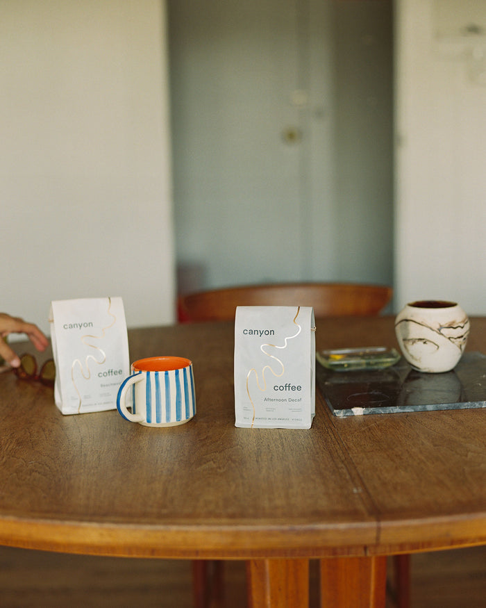 A bag of Afternoon Decaf Coffee by Canyon Coffee at home with ceramic mugs on a wood dining table