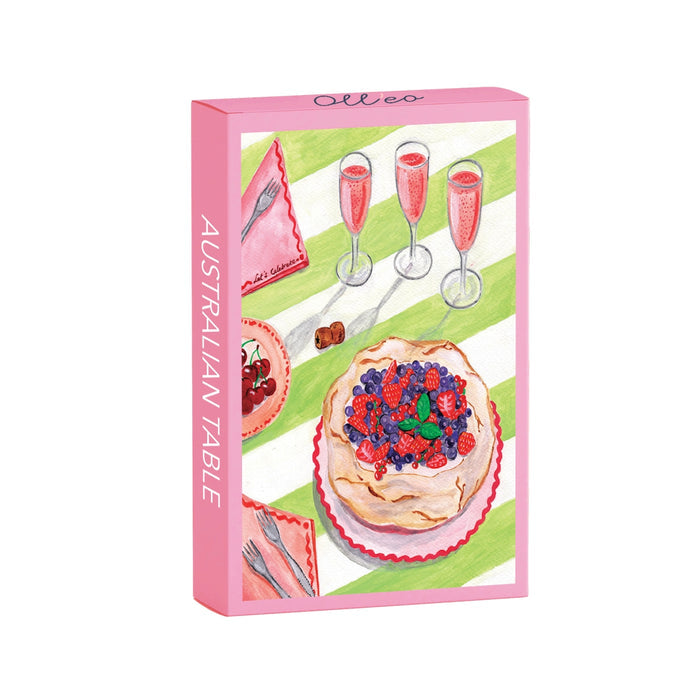 The Australian Table | 99 Piece Jigsaw Puzzle by Olleo Puzzles features a boxed set with pavlova topped with berries, three glasses of pink drink, and utensils on a green and white tableclothβan authentic Australian scene.