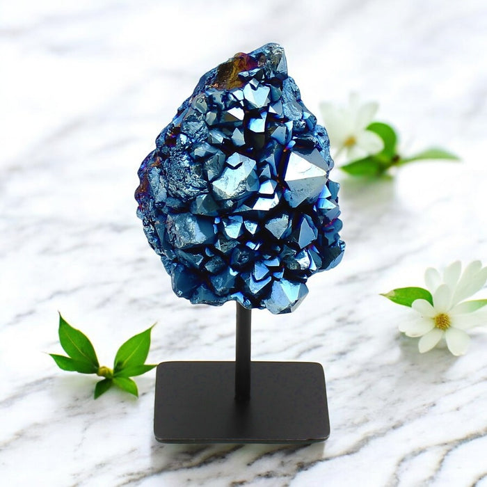 Blue Aura Geode on Stand on a stand with white flowers and green leaves on a marble surface