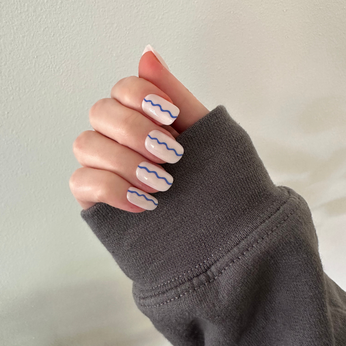 Simple Squiggle | Short | Squoval - Tab Press-On nails with neutral base and blue wavy line design on hand against light background