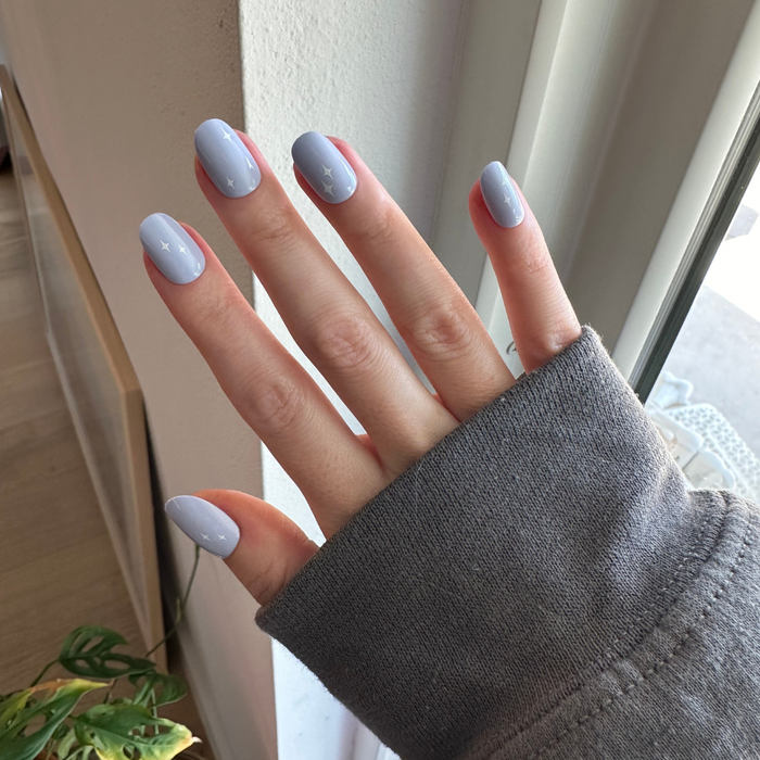 Sparkle Accent | Short | Round - Tab Press-On showing hand with light blue mani and white star sparkles near window light