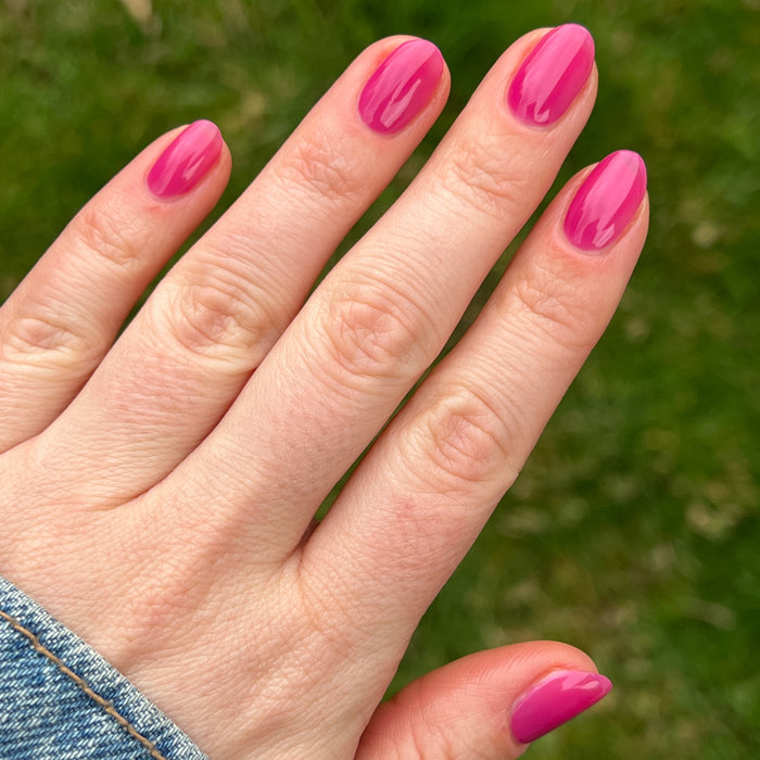 Hand displaying glossy nails painted with This Lettuce is Radicchio magenta-purple gel polish by Olive and June outdoors
