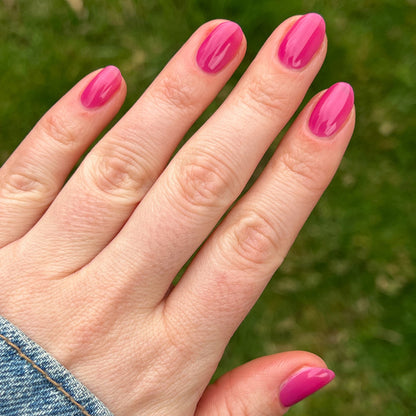 Hand displaying glossy nails painted with This Lettuce is Radicchio magenta-purple gel polish by Olive and June outdoors