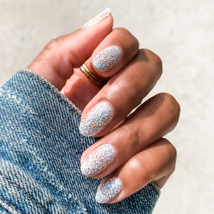 Hand with nails covered in Olive and June Exclamation Point silver holographic glitter polish for a sparkling manicure