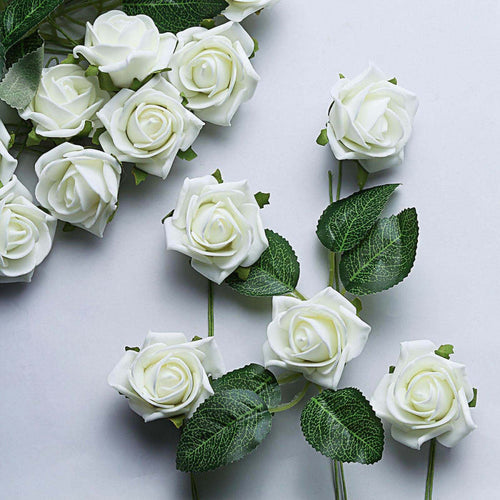 Artificial white roses with green leaves on a plain backdrop.