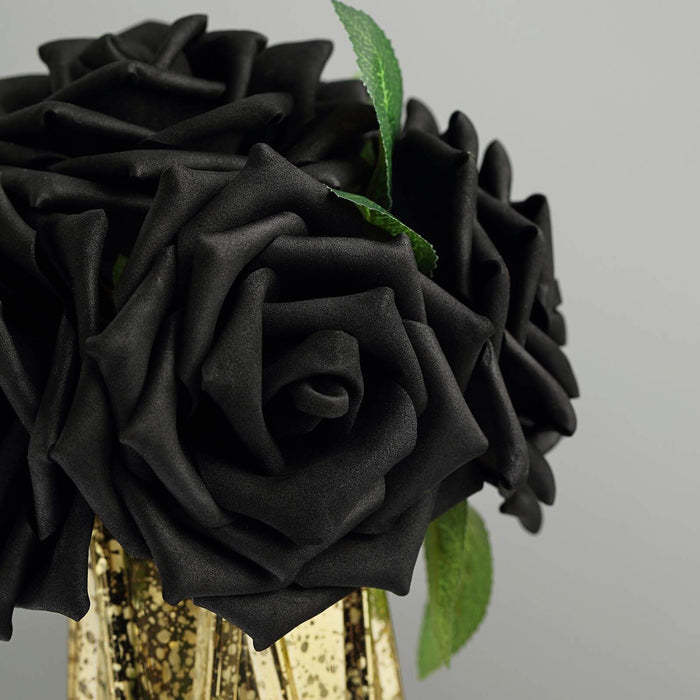 Black artificial roses in a gold vase with green leaves.