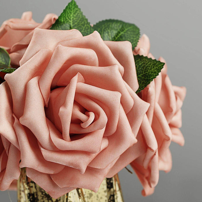 Pink artificial roses in a decorative vase with green leaves.
