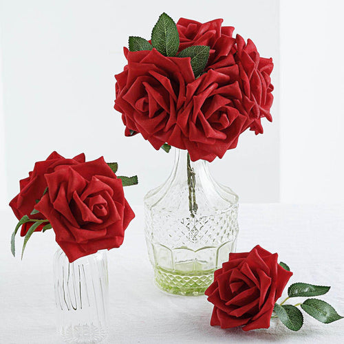 Red artificial roses in glass vases on a white table.
