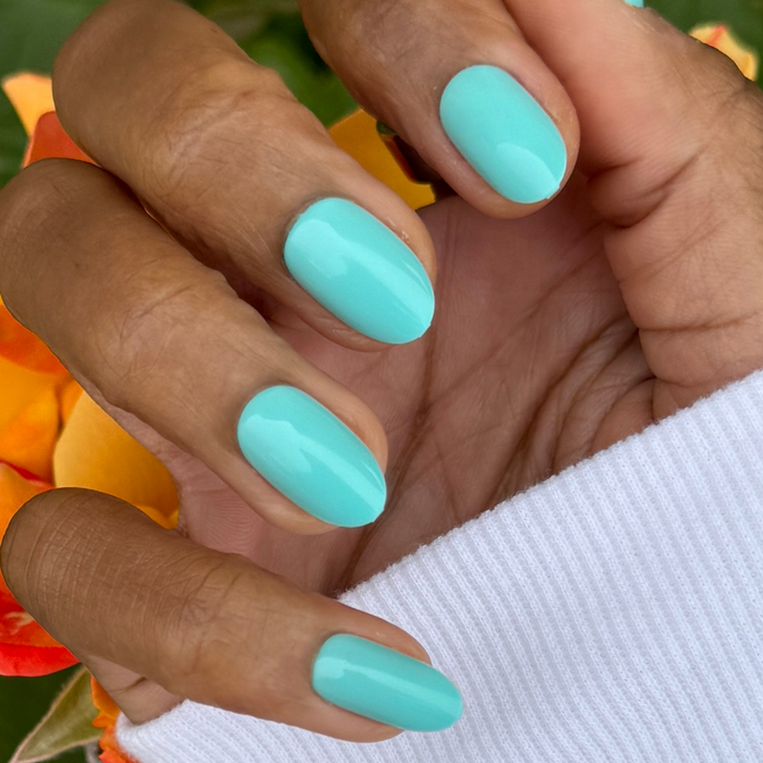 All Manis on Deck | Medium | Oval - Tab Press-On nails in bright aquatic blue-green shade shown on hand with floral background