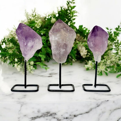 Three amethyst crystal points on stands with a floral background
