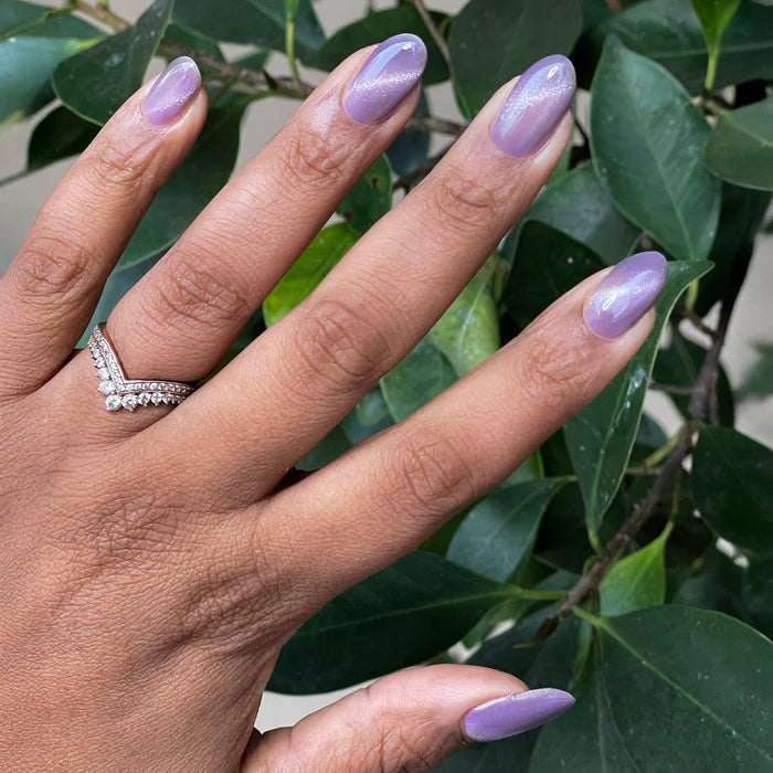 Hand with nails featuring Amethyst Velvet - Gel pastel lavender magnetic gel polish with subtle shimmer against green leaves background