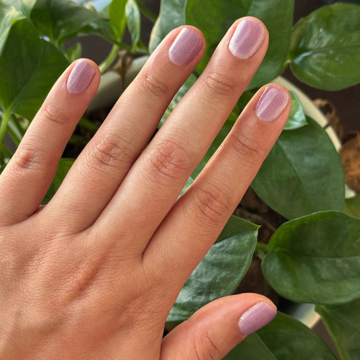 Hand showing nails painted with Amethyst Velvet - Gel pastel lavender magnetic polish with subtle shimmer by greenery background