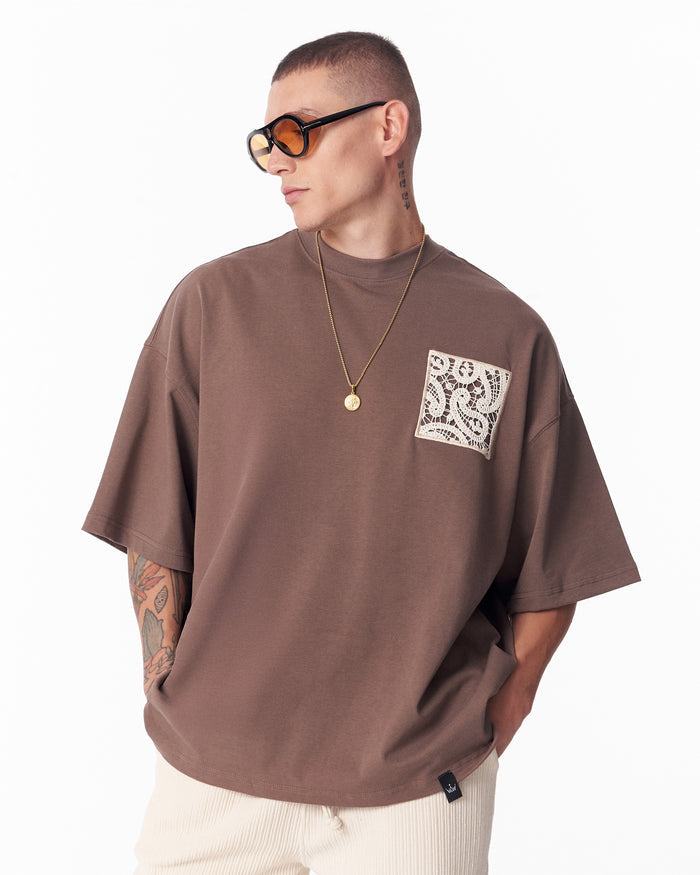 Martin Valen brown T‑shirt worn in profile, visible lace applique chest pocket and pendant necklace