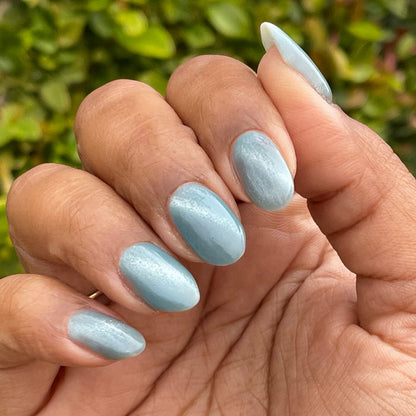 Fingernails painted with Aqua Velvet - Gel bright pastel blue magnetic gel polish showing shimmering velvet finish against natural greenery background