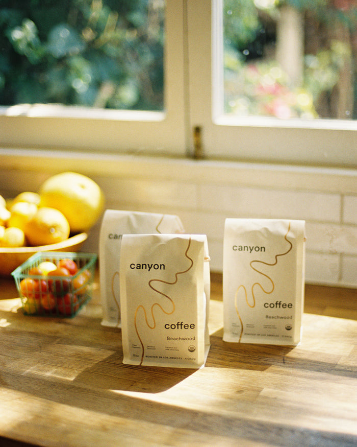 three basgs of Beachwood USDA organic coffee by Canyon Coffee in the kitchen with a bowl of fruit