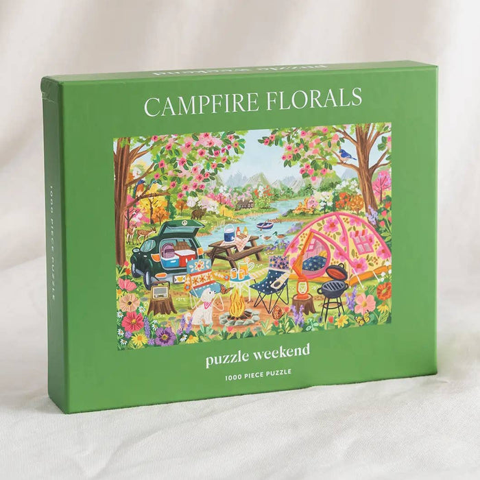 The green box labeled “Campfire Florals | 1,000 Piece Jigsaw Puzzle” by Puzzle Weekend features an illustrated picnic scene with a tent, car, food, and flowers; inside is a 1,000-piece camping-themed puzzle.
