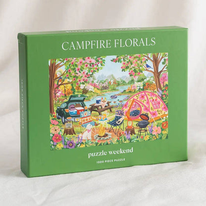The green box labeled “Campfire Florals | 1,000 Piece Jigsaw Puzzle” by Puzzle Weekend features an illustrated picnic scene with a tent, car, food, and flowers; inside is a 1,000-piece camping-themed puzzle.