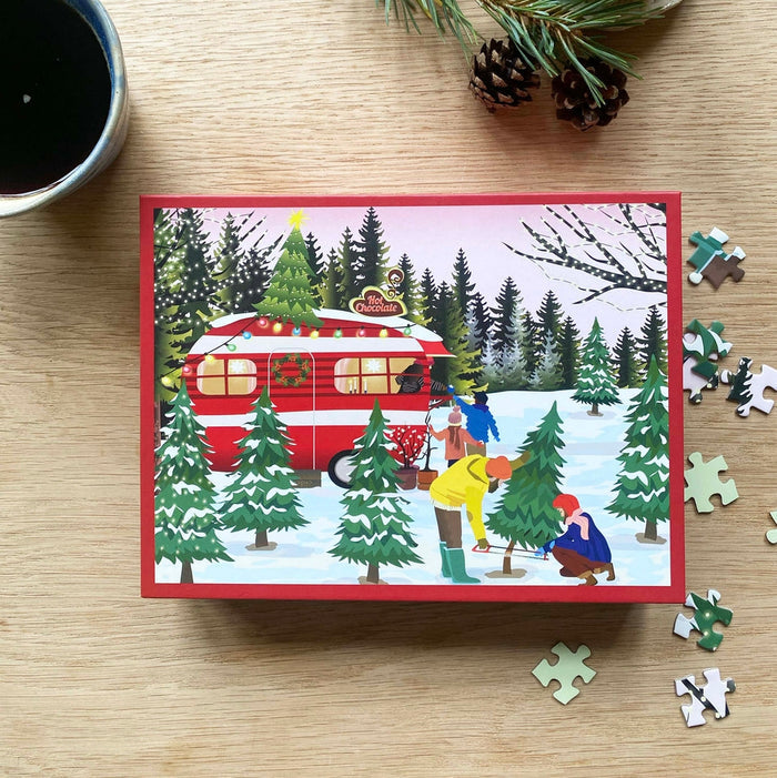 Experience the joyful spirit of a Christmas market adventure with the Caravan | 300 Piece Jigsaw Puzzle by ViSSEVASSE, featuring a heartwarming scene of people cutting a Christmas tree in a snowy forest near a red camper, surrounded by festive holiday decorations and loose puzzle pieces.