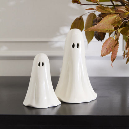 Two white ghost figurines on a dark surface with a blurred background