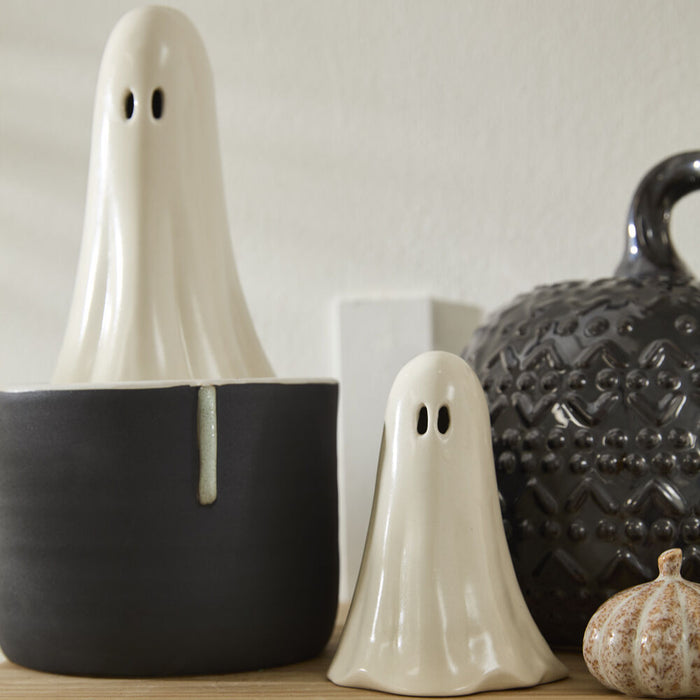 Two ghost-shaped decorative items on a shelf with a neutral background