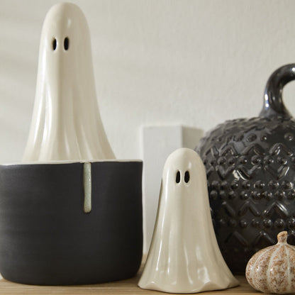 Two ghost-shaped decorative items on a shelf with a neutral background