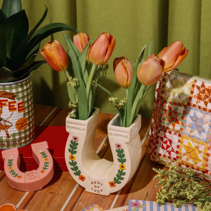 Decorative items including tulips in a shoe-shaped vase on a wooden surface with a green curtain background.