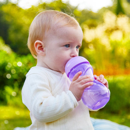 A young child with light hair drinks from a Clik-It Soft Spout Sippy Cup (2 Pack) | Purple / Aqua outdoors on a sunny day, with green foliage softly blurred in the background.