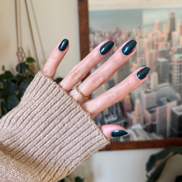 Hand with medium-length nails painted in deep emerald green shiny polish Dancing Green - Gel against blurred city background