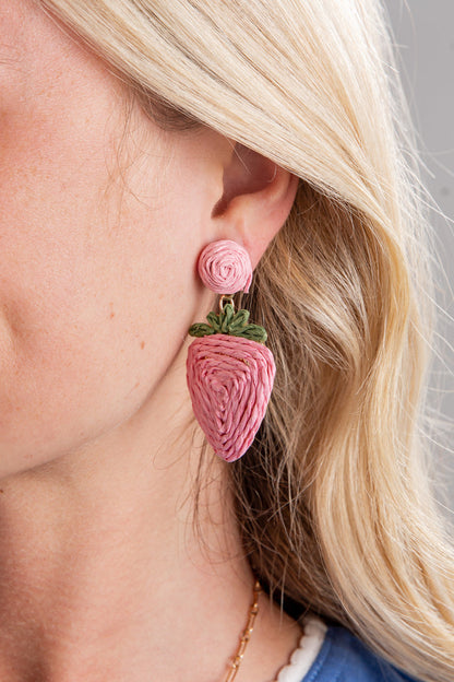 Close-up of a person wearing pink strawberry-shaped earrings with a rose detail.