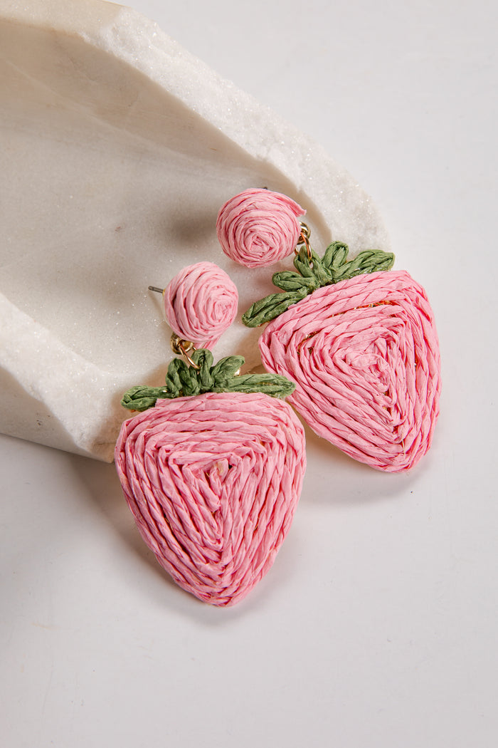 Pink strawberry-shaped earrings with green leaves on a white surface