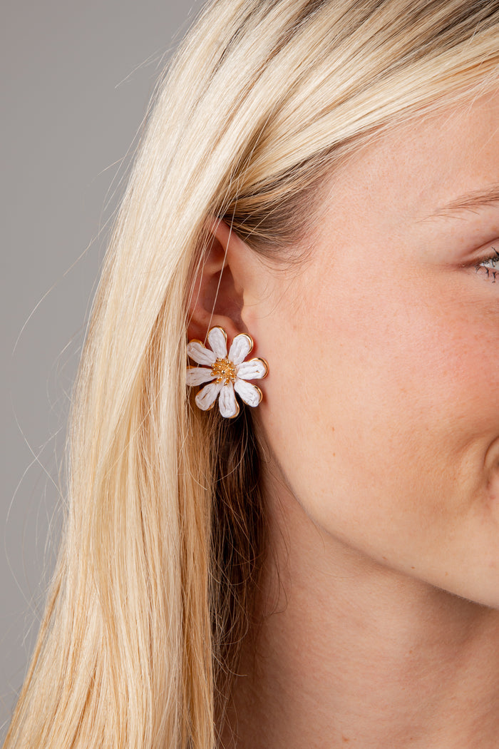 Close-up of a woman wearing a white flower earring with a gold center against a neutral background