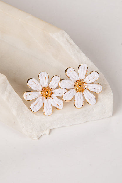 White daisy earrings with gold centers on a beige fabric background