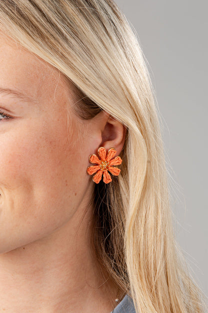 Close-up of a person wearing an orange floral earring against a neutral background