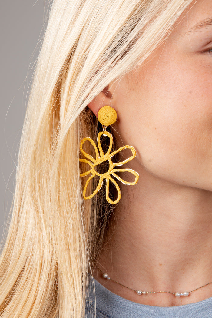 Close-up of a person wearing gold flower-shaped earrings with a neutral background