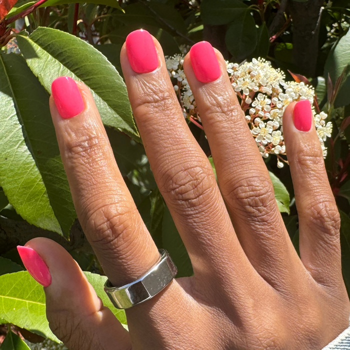 Flamingo | Extra Short | Squoval - Tab Press-On nails in bright neon pink on hand with white flowers and green leaves background