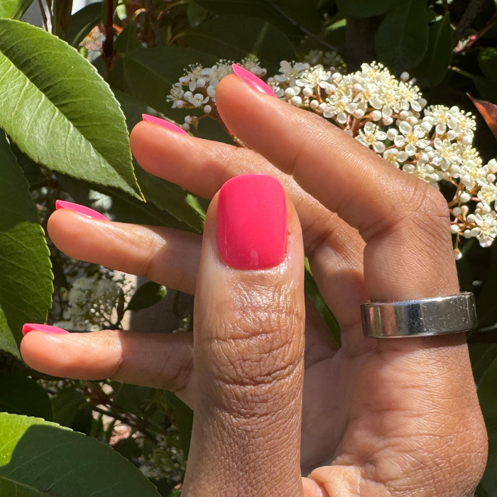 Flamingo | Extra Short | Squoval - Tab Press-On nails in bright nearly neon pink on hand with white flowers in natural light