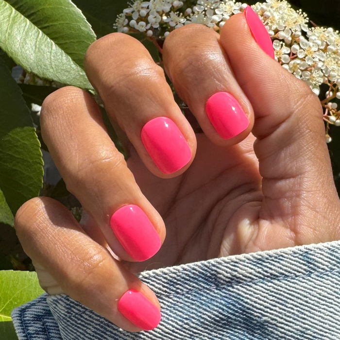 Flamingo | Extra Short | Squoval - Tab Press-On nails in bright neon pink on hand outdoors with white blossoms and greenery