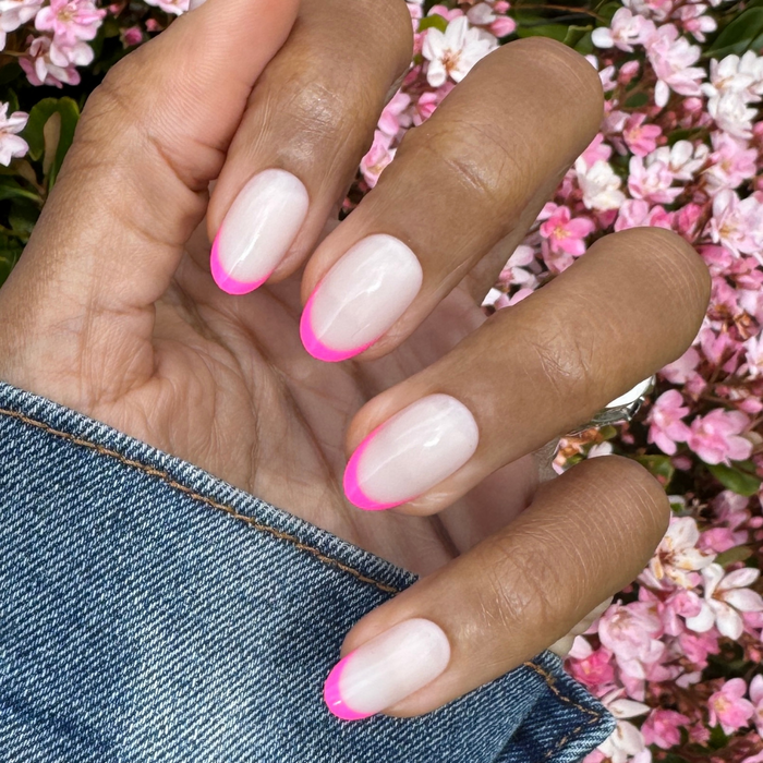 Flamingo French | Medium | Oval - Tab Press-On nails with neutral base and bright pink tips on hand outdoors with pink flowers