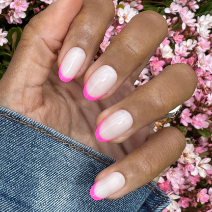 Flamingo French | Medium | Oval - Tab Press-On nails with neutral base and bright pink tips on hand outdoors with pink flowers