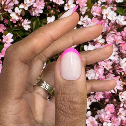 Flamingo French | Medium | Oval - Tab Press-On nails with neutral base and neon pink tips held near pink flowers outdoors