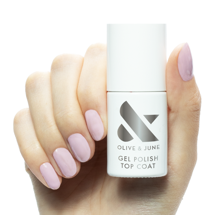 Hand holding Gel Top Coat bottle with glossy soft pink gel polished nails for at home manicure care