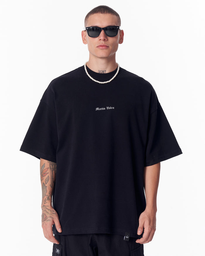 Martin Valen Gothic Depth black oversized T-shirt walking away, rear view showing large printed patch and black cargo pants