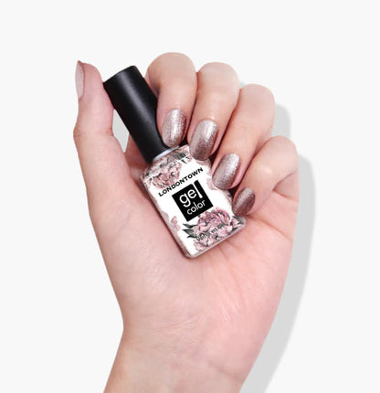 Hand with glittery nail polish holds a bottle labeled "Kissed by Rose Gold" from LONDONTOWN, featuring a floral design.