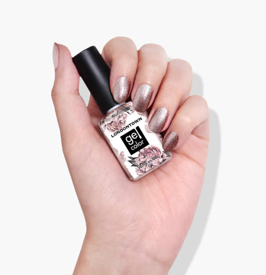 Hand with glittery nail polish holds a bottle labeled "Kissed by Rose Gold" from LONDONTOWN, featuring a floral design.