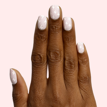 Lightning Strike | Extra Short | Squoval - Tab Press-On neutral nails with white lightning bolt design on hand against pale pink background