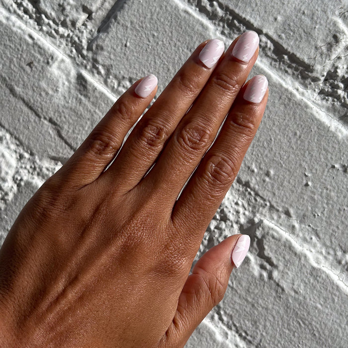 Lightning Strike | Extra Short | Squoval - Tab Press-On nails with light neutral polish and faint lightning bolt design on hand against textured white wall