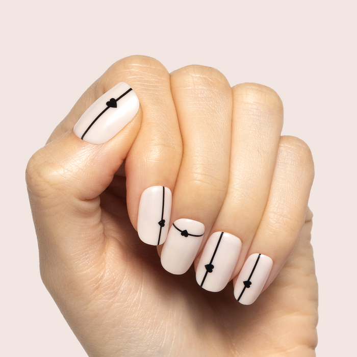 Linear Hearts | Short | Squoval - Tab Press-On neutral nails with thin black lines and small heart accents on a hand against pale background