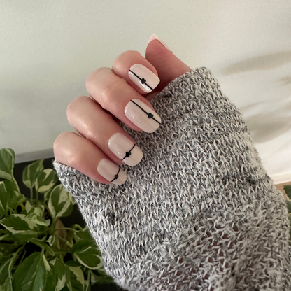 Linear Hearts | Short | Squoval - Tab Press-On neutral nails with black linear details and heart accents on hand in cozy knit sleeve