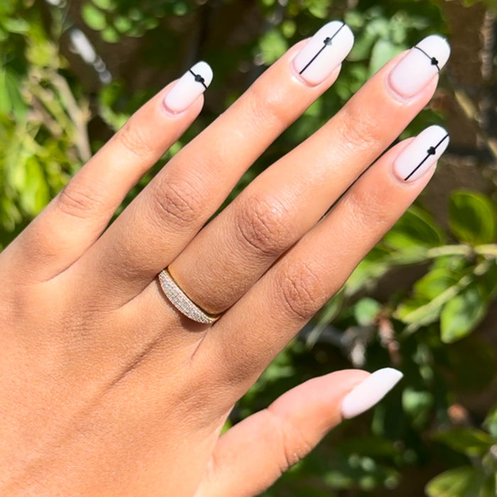 Linear Hearts | Short | Squoval - Tab Press-On neutral nails with thin black lines and tiny heart details on hand outdoors in sunlight