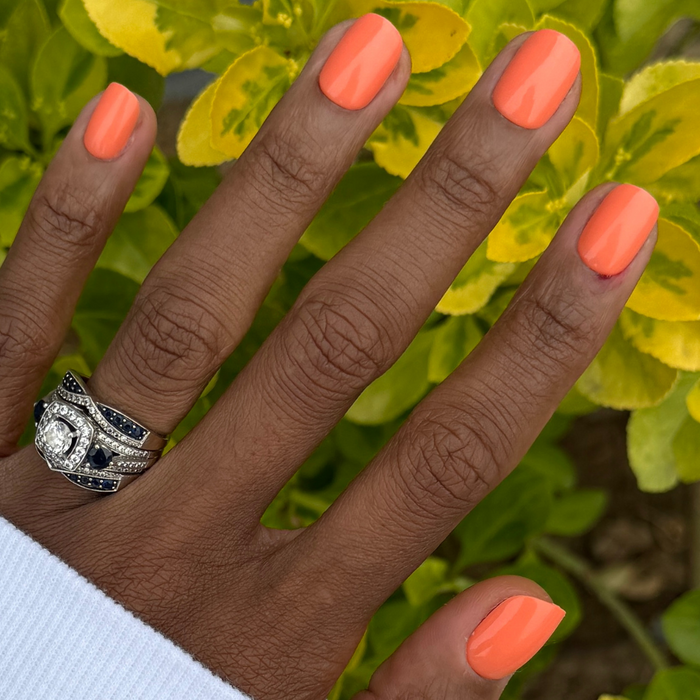 Lobster | Extra Short | Squoval - Tab Press-On nails in bright orangey red pink shown on hand outdoors with foliage background